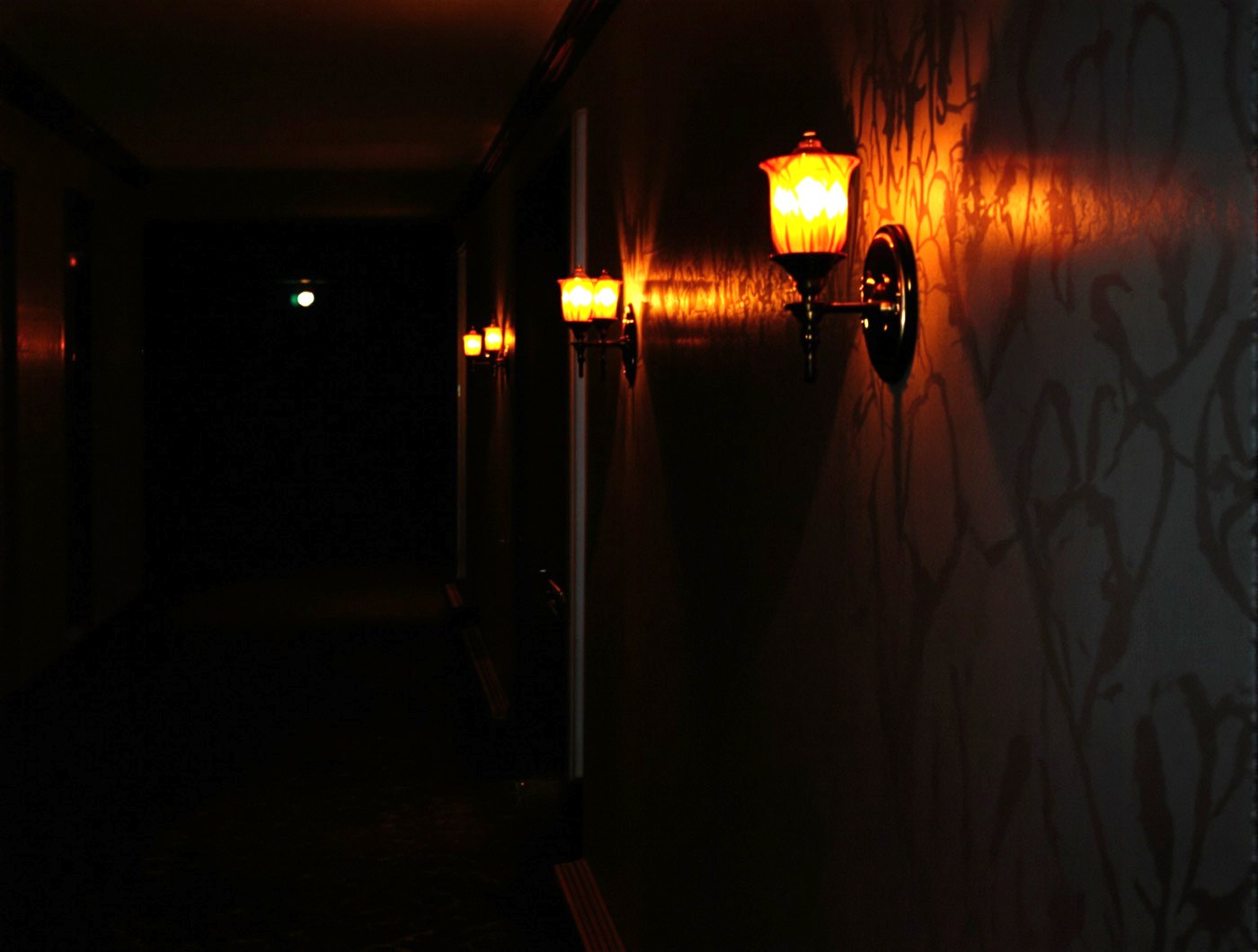 A dim hotel corridor at night lit by a row of warm amber wall sconces.